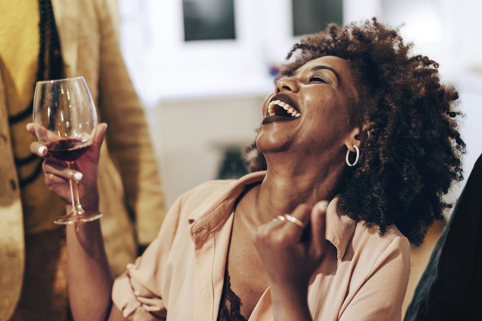 smiling happy african lady at table   african american woman laughing at party   young female person holding glass of wine at dinner