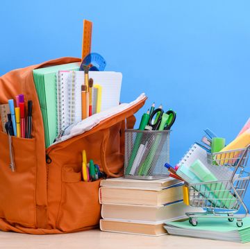 orange school backpack full of school supplies and a supermarket basket with office supplies on a blue background.