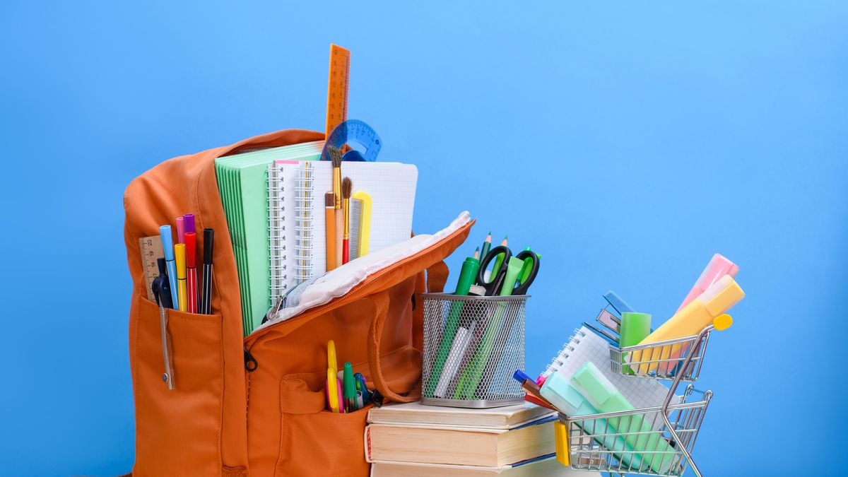 orange school backpack full of school supplies and a supermarket basket with office supplies on a blue background.