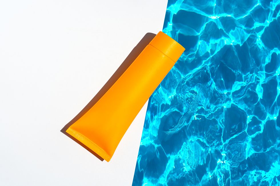 orange tube with suntan lotion, cosmetic face cream or hand cream, shower gel, shampoo against the background of blue turquoise water with waves from the swimming pool