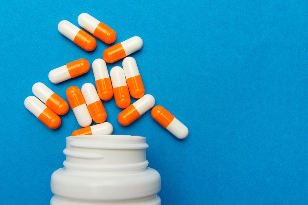 orange white capsules pills were poured from a white bottle on a blue background medical background, template