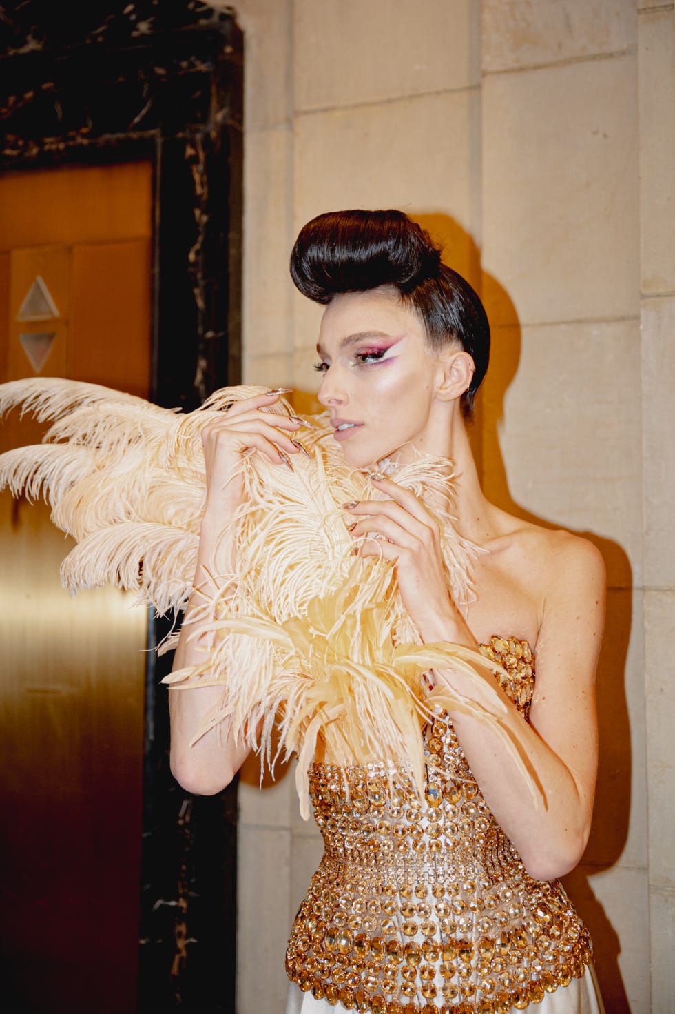 A person adorned with a feather accessory and a bejeweled outfit in a luxurious setting