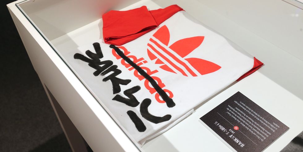a banksy signature is spraypainted over an article of clothing sitting in a white display case