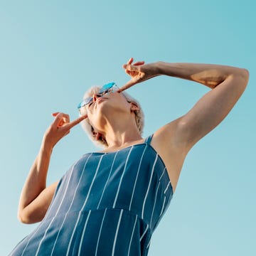 Woman in a blue jumpsuit striking a playful pose, pointing at her stylish glasses, under a bright blue sky, radiating fun and confidence. woman in a blue jumpsuit striking a playful pose, pointing at her stylish glasses, under a bright blue sky, radiating fun and confidence