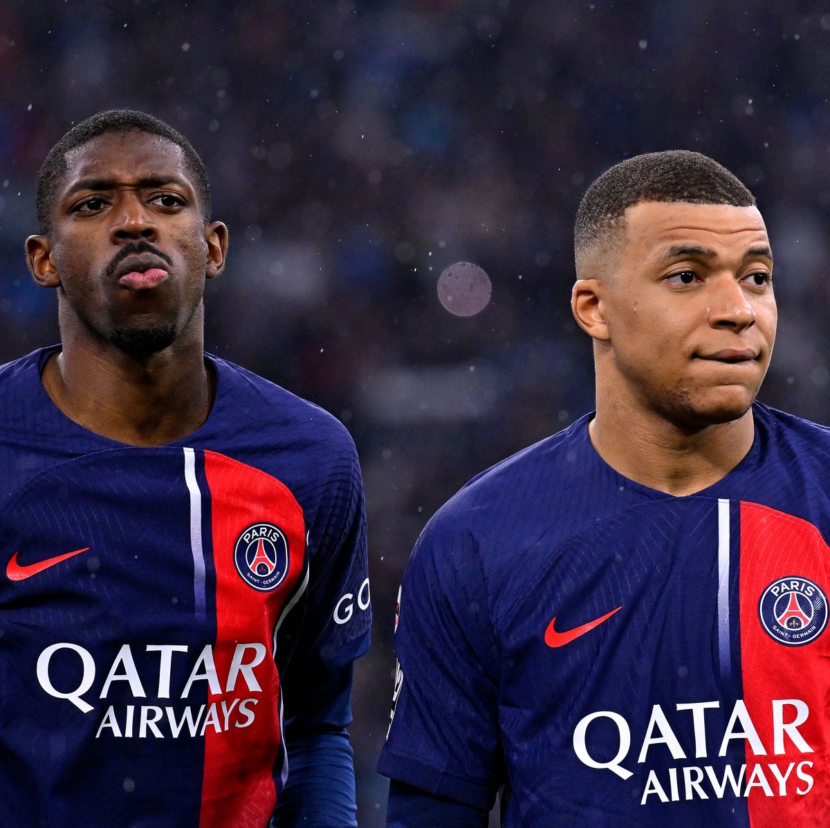 paris saint germain players ousmane dembele and kylian mbappe stand on a football pitch in the rain