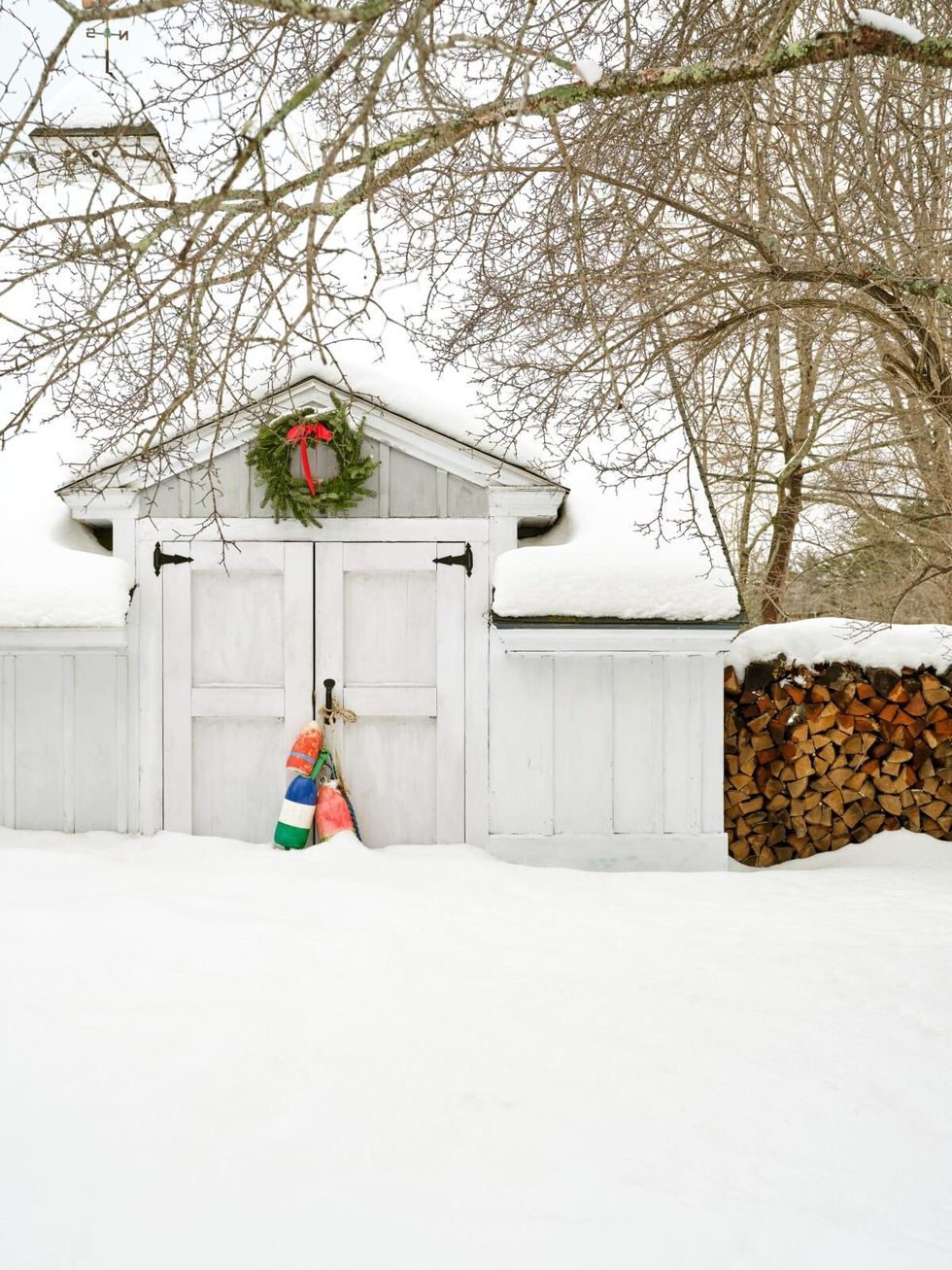 white barn with red and green bouys tied to the door in the snow