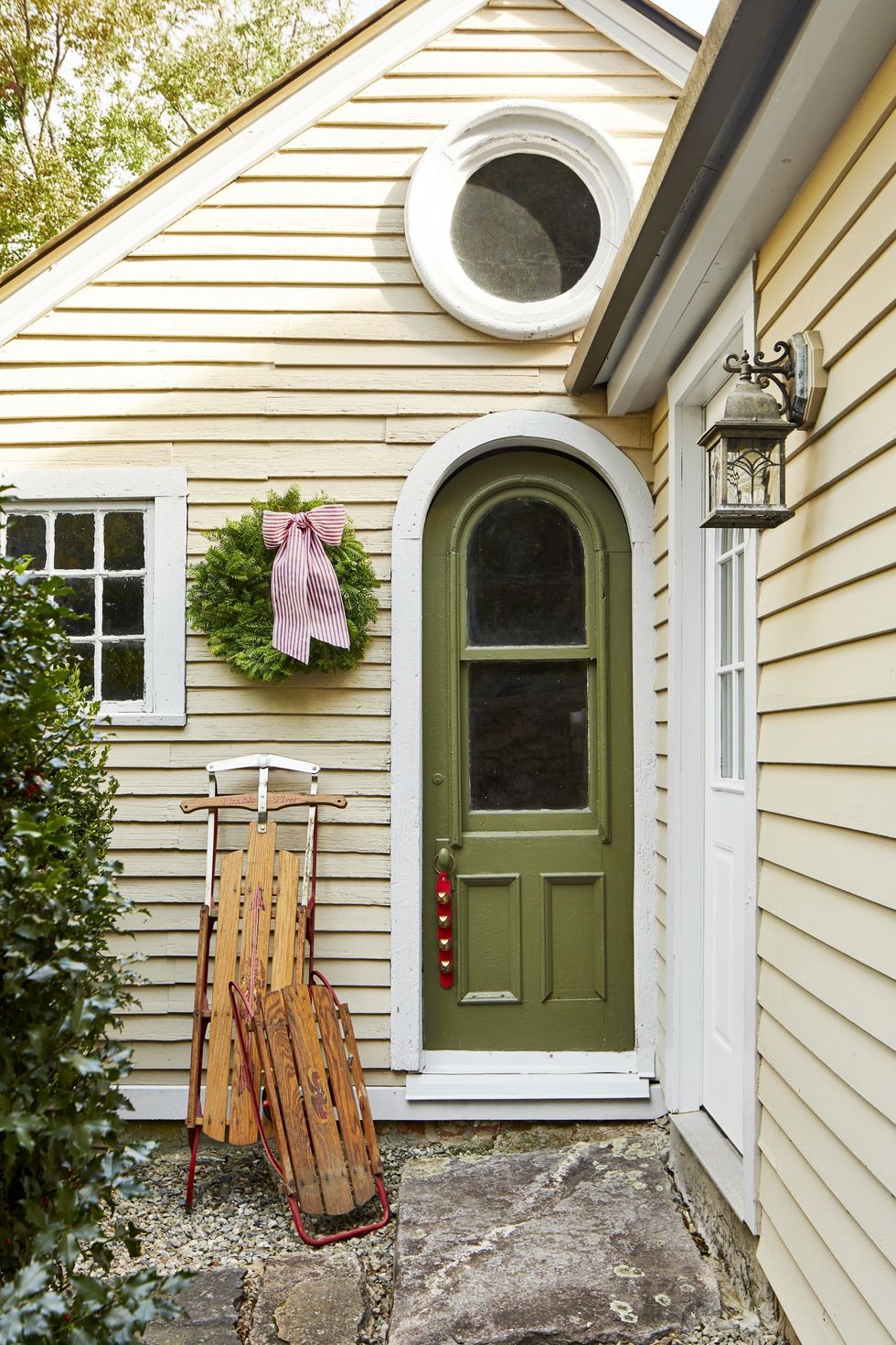 Front door with an antique sleigh, a simple wreath with striped ribbons and a green door decorated with jingle bells