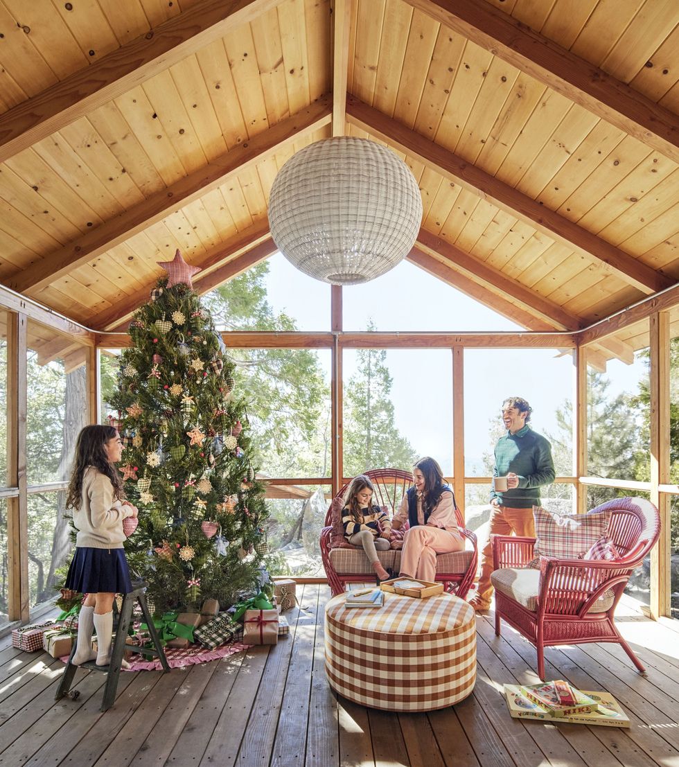 Heather Taylor's family decorates an outdoor Christmas tree on the screened porch of a rustic cabin with red wicker chairs and a plaid ottoman