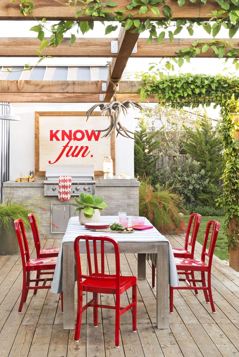 stone grill in a backyard with wood dining table and red chairs in outdoor kitchen ideas