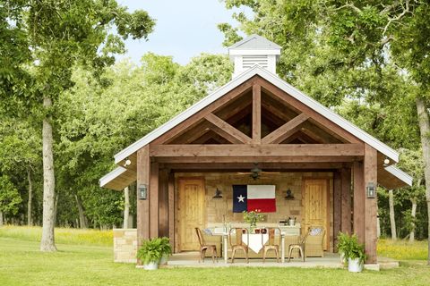 outdoor kitchen ideas that include a wood beam pavilion with a texas state flag hanging and a set of table and chairs