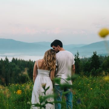 outdoors romantic portrait of young couple beautiful summer landscape of mountains with fog, hills, forest and green meadow of yellow wild flowers