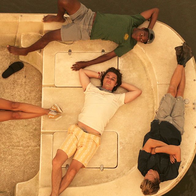 a still from outer banks on netflix the image contains three characters laying out on a boat one is looking upward, while two are looking toward a central character