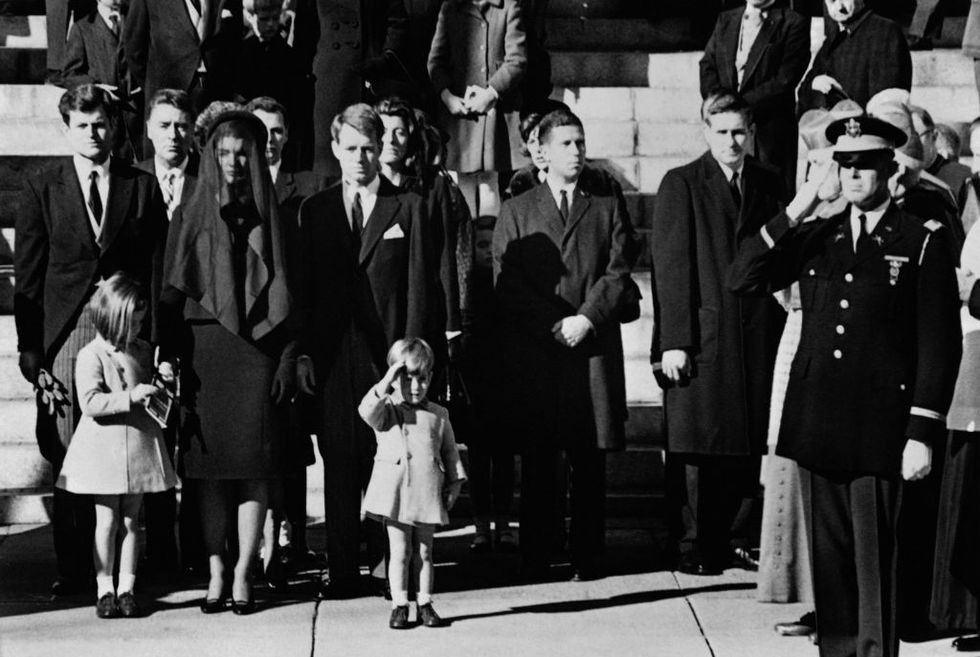 caroline kennedy, jacqueline kennedy, john f kennedy jr and other kennedy family members stand on a sidewalk
