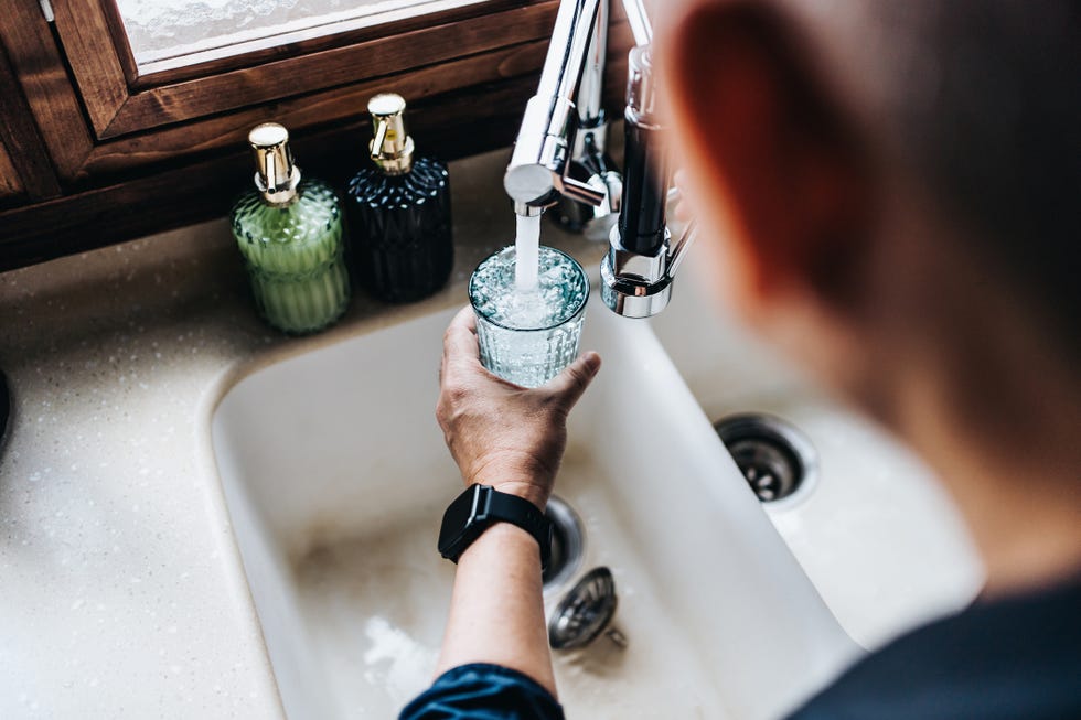 over the shoulder view of senior asian man filling a glass of filtered water right from the tap in the kitchen at home