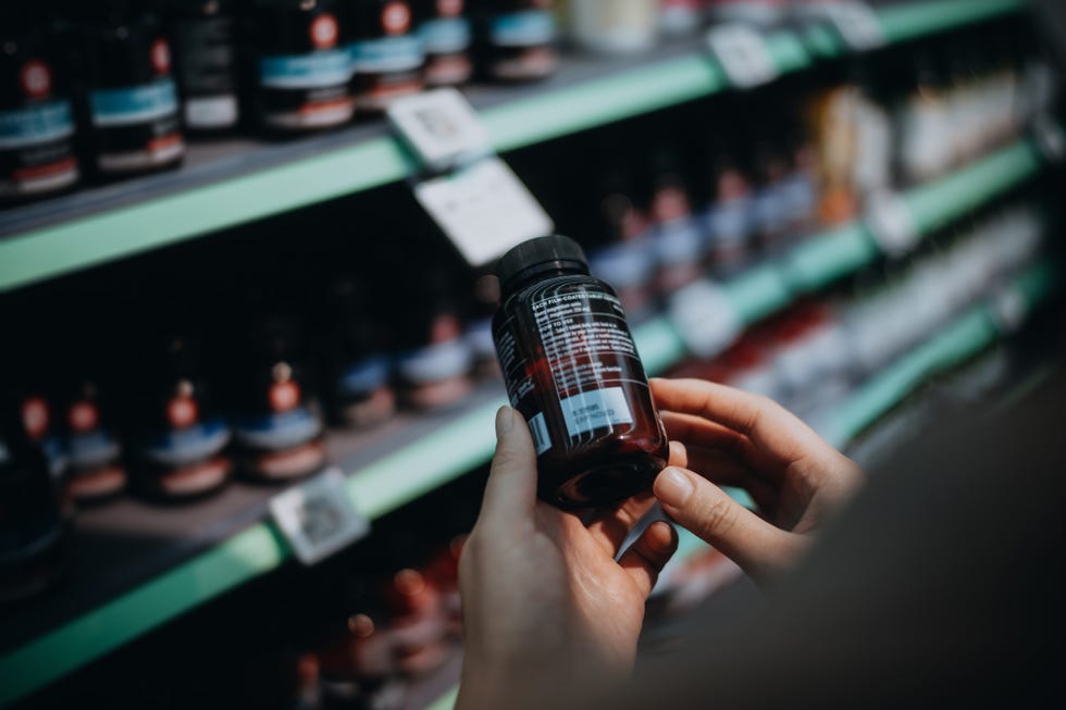 over the shoulder view of woman browsing through medical products and reading the label on a bottle of medicine in front of the shelves in a pharmacy healthcare, medication and people concept