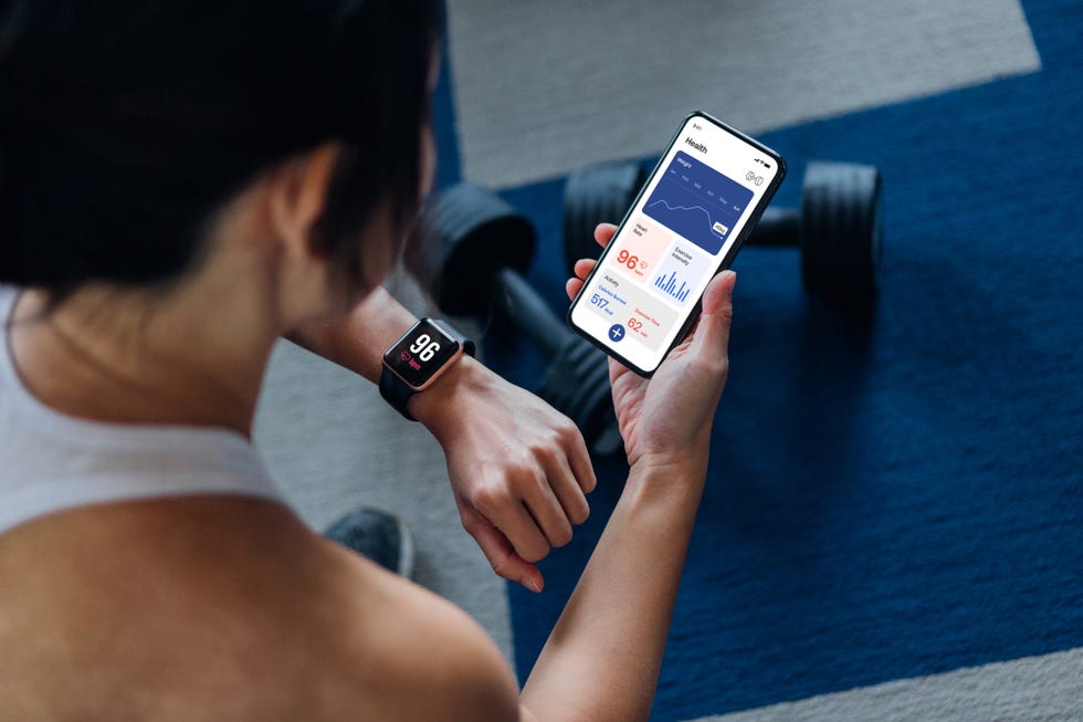 over the shoulder view of young active woman using exercise tracking app on smartphone to monitor her training progress after exercising at home