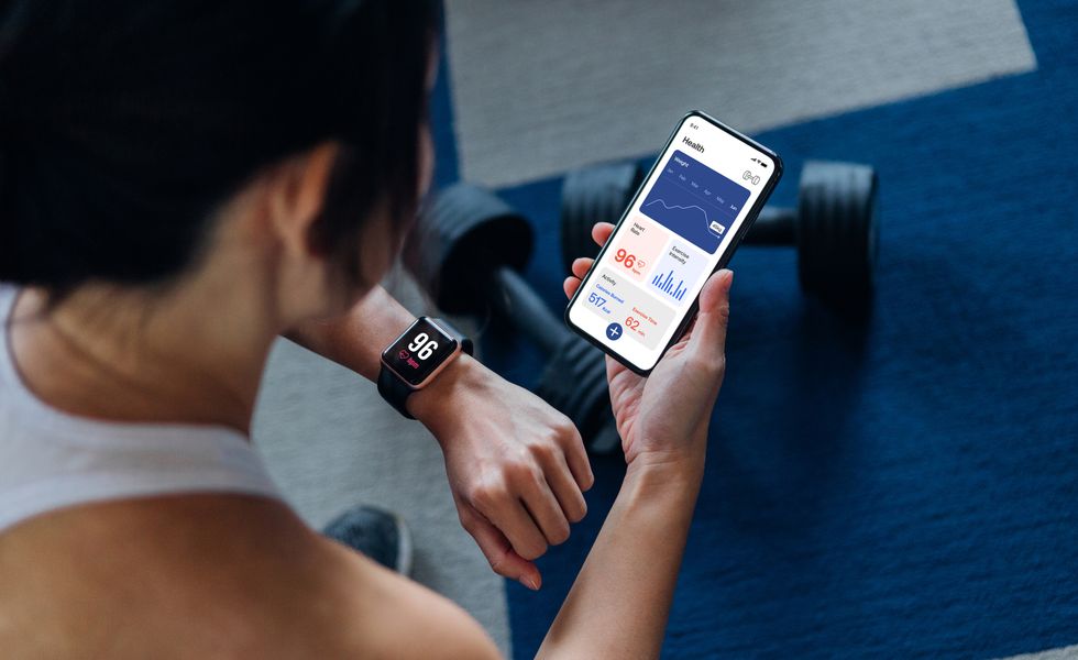 over the shoulder view of young active woman using exercise tracking app on smartphone to monitor her training progress after exercising at home