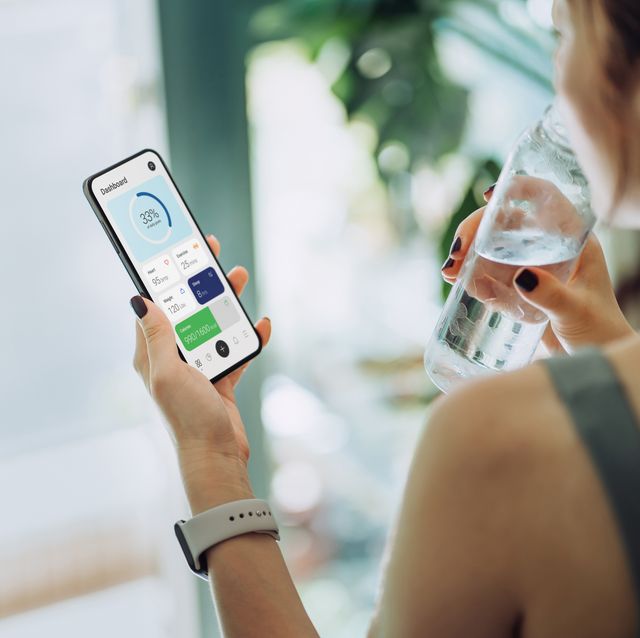 woman refreshing with water and using calorie counting app on smartphone for good housekeepings best calorie counting apps