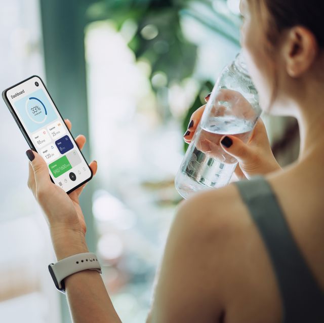 woman refreshing with water and using calorie counting app on smartphone for good housekeepings best calorie counting apps