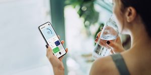 woman refreshing with water and using calorie counting app on smartphone for good housekeepings best calorie counting app