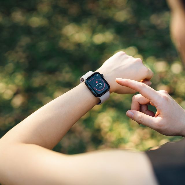 over the shoulder view of young asian sports woman resting after working out outdoors in green park, measuring heart rate on her smartwatch. health and fitness training with technology. wearable technology. healthy living lifestyle, sports routine concept