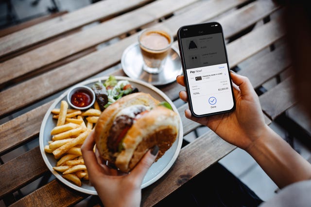 over the shoulder view of young asian woman shopping online on smartphone and making payment online with credit card while enjoying lunch in a restaurant lifestyle and technology comfortable and simple online shopping experience
