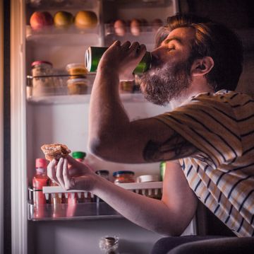 young bearded man having a beer and late night snack in front of the refrigerator