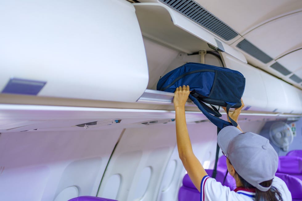 traveler woman open overhead locker on airplane, passenger put cabin bag cabin on the top shelf.