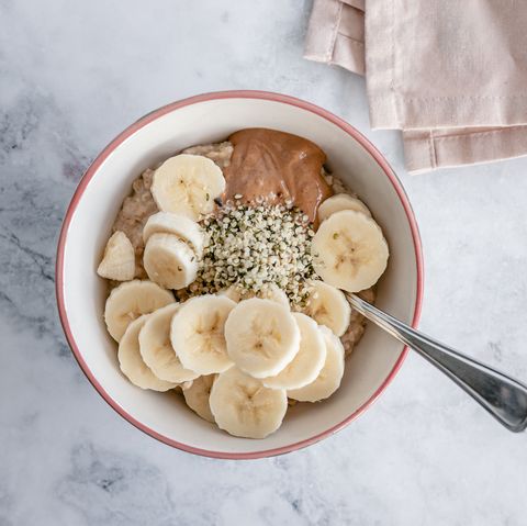 overhead view of a bowl of oatmeal with slices of banana, nut butter and hemp seeds