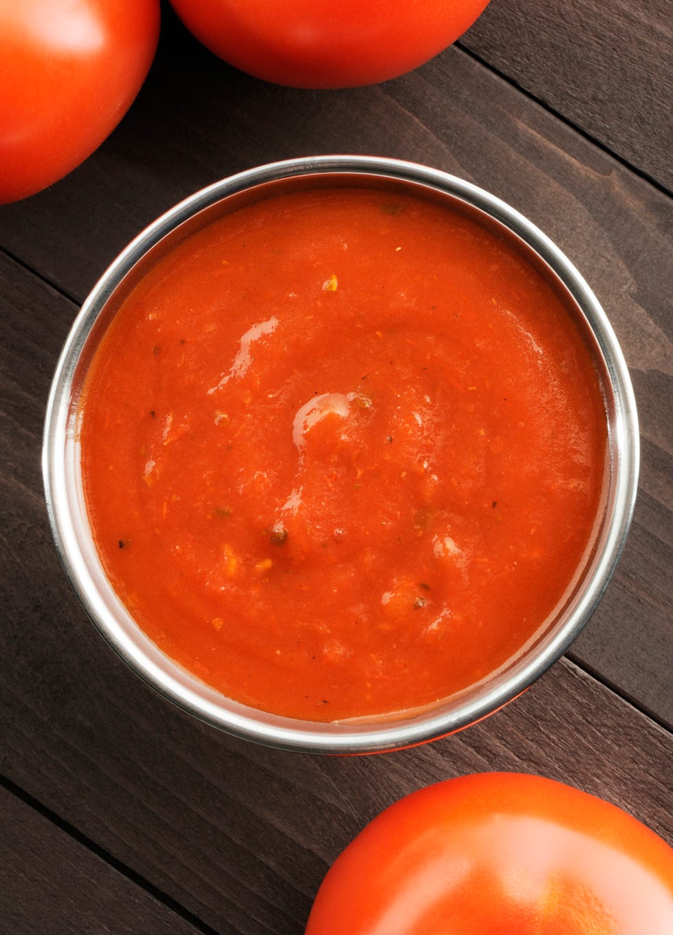 Overhead view of a bowl of tomato sauce next to tomatoes
