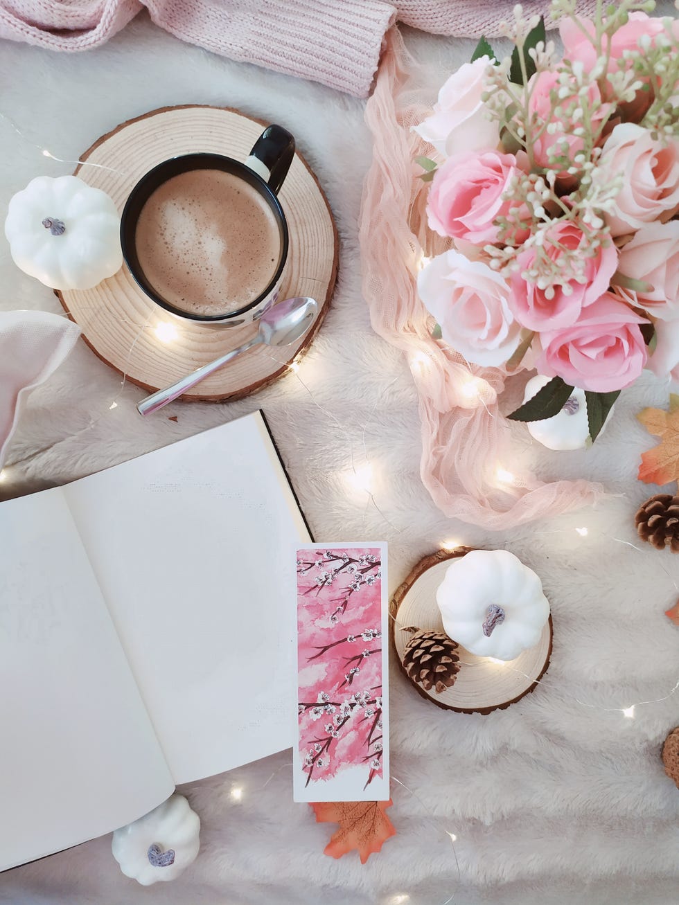 overhead view of a cup of coffee with flowers, fairy lights, open notebook and autumnal decorations