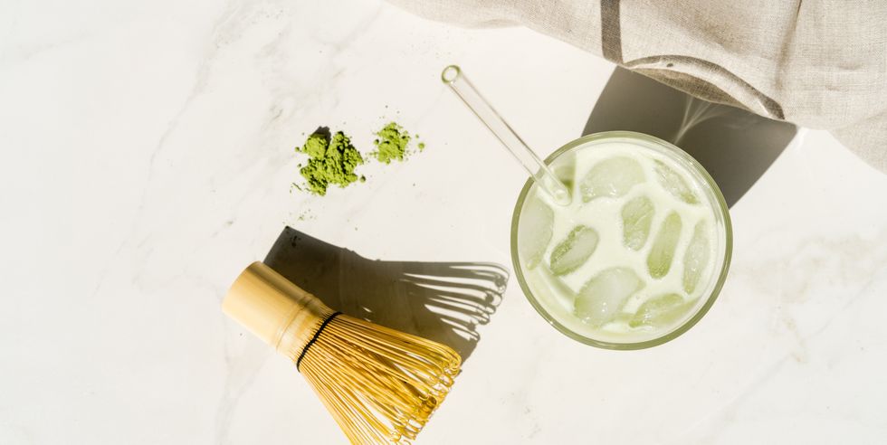 overhead view of an iced matcha green tea drink next to matcha powder, bamboo whisk and spoon