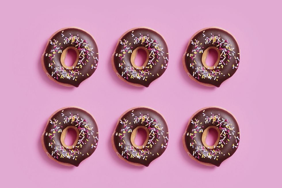 overhead view of chocolate donuts with sprinkles arranged on pink background