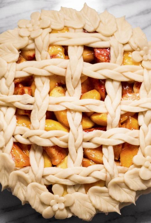Overhead view of floral peach pie on marble counter