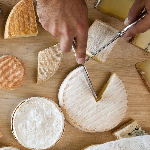 overhead view of hands cutting multiple cheeses