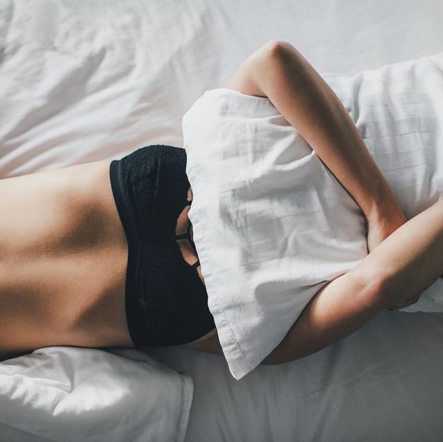 overhead view of sensuous woman covering face with pillow on bed