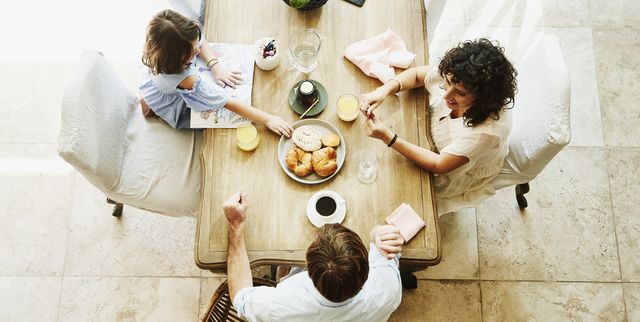 overhead view of smiling wife and husband sharing breakfast with daughter at dining room table