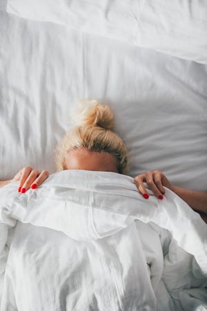 Overhead view of woman covering face with blanket on bed