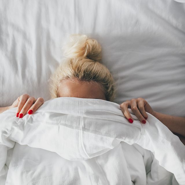 Overhead view of woman covering face with blanket on bed
