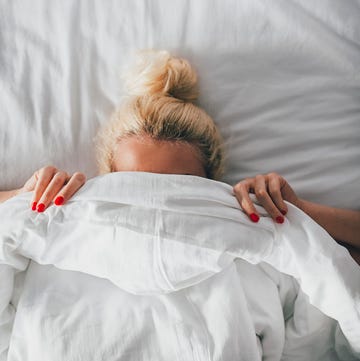 overhead view of woman covering face with blanket on bed