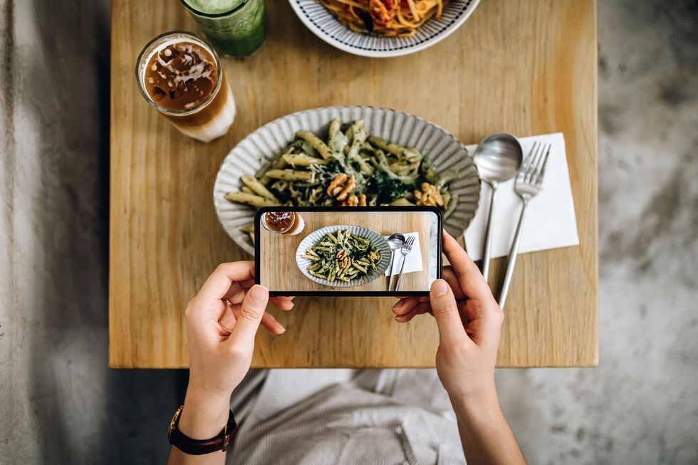 overhead view of woman's hand taking a photo of freshly served food with smartphone while having meal with friend in a restaurant