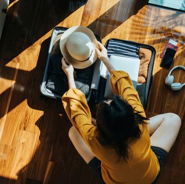 overhead view of young asian woman sitting on the floor in her bedroom, packing a suitcase for a trip. getting ready for a vacation. traveller's accessories. travel and vacation concept