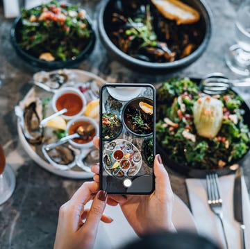 overhead view of young woman taking photos of scrumptious and delicious meal on dining table with smartphone before eating it in restaurant eating out lifestyle camera eats first culture