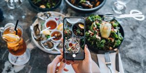 overhead view of young woman taking photos of scrumptious and delicious meal on dining table with smartphone before eating it in restaurant eating out lifestyle camera eats first culture