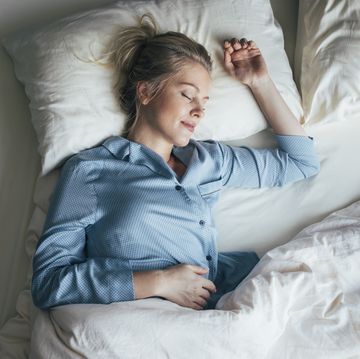 sound asleep overhead waist up shot of a pretty blonde woman in blue pyjamas sleeping on a king size bed
