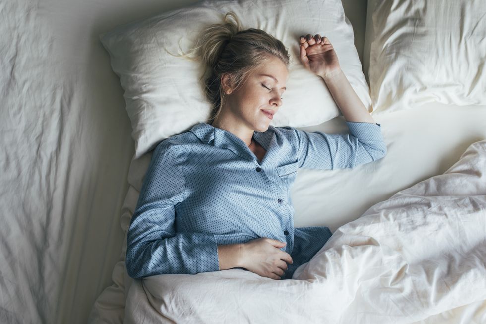 sound asleep overhead waist up shot of a pretty blonde woman in blue pyjamas sleeping on a king size bed