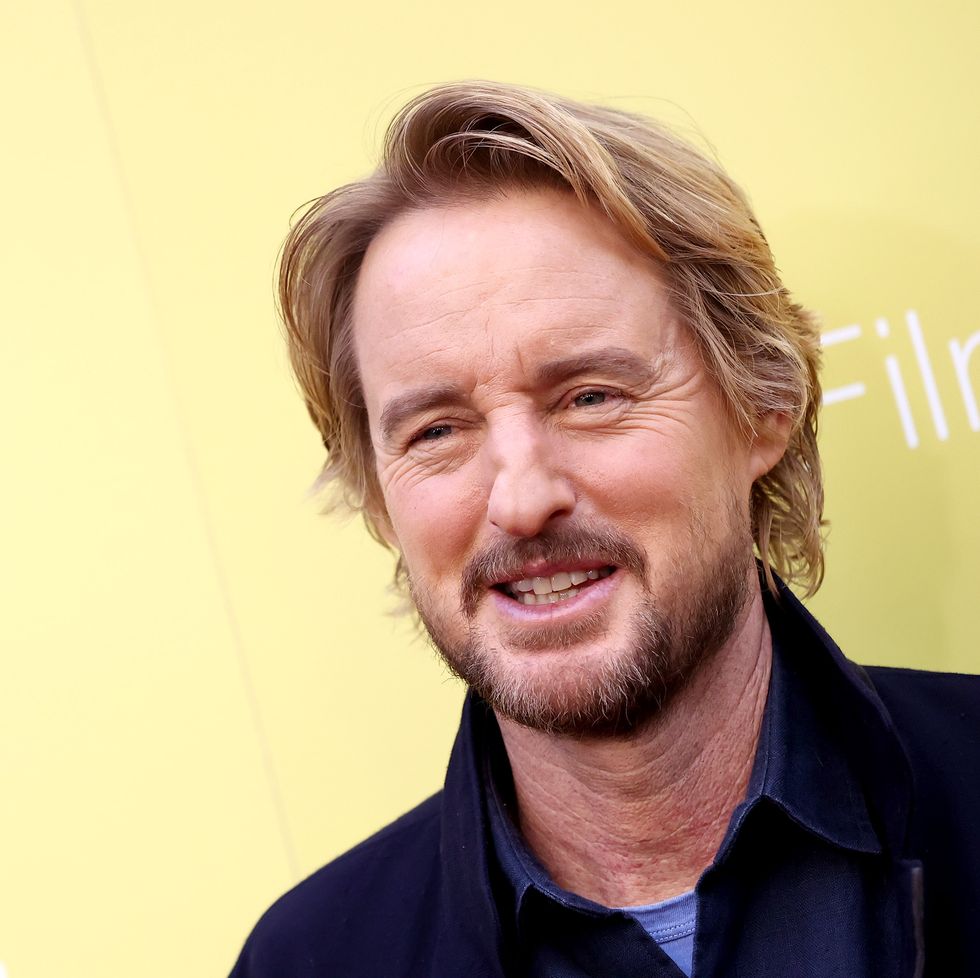 owen wilson smiling and looking off camera with a yellow wall in the background