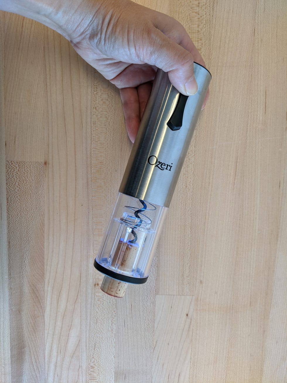a hand is holding an electric wine opener which reveals a cork being ejected from the screw