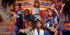 a group of kids stands and sits in front of a fake marque advertising the all new mickey mouse club
