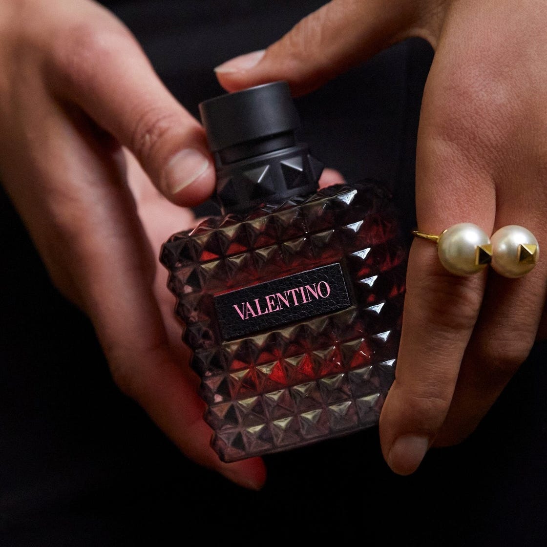valentino fragrance bottle held in a hand with a pearl ring